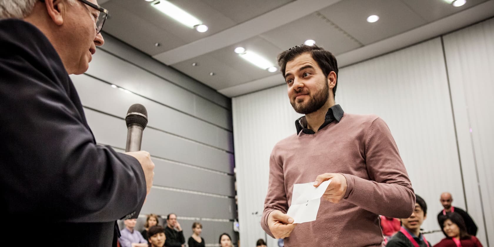 A man hands a document or envelope to another man at an event.