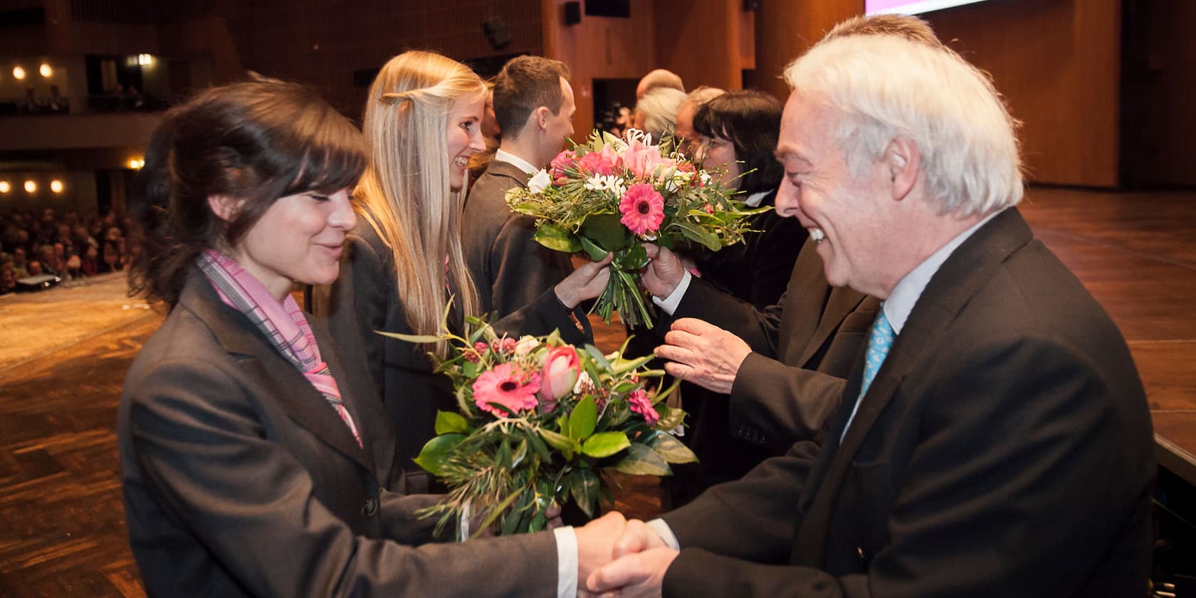 People on a stage exchanging bouquets of flowers.