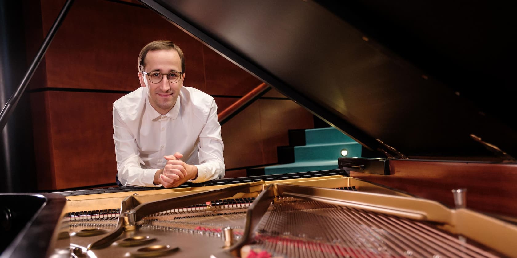 Man in white shirt leaning over the open grand piano.