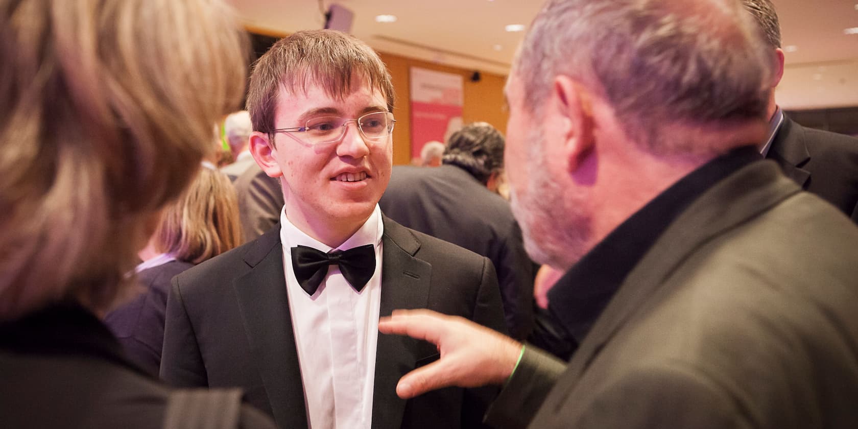 Person in a suit and bow tie talking to another person at an event.