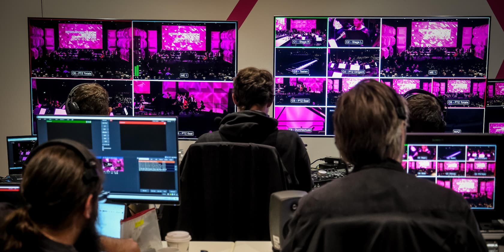 Several people monitor screens in a control room during an event. The screens display various shots of the event.