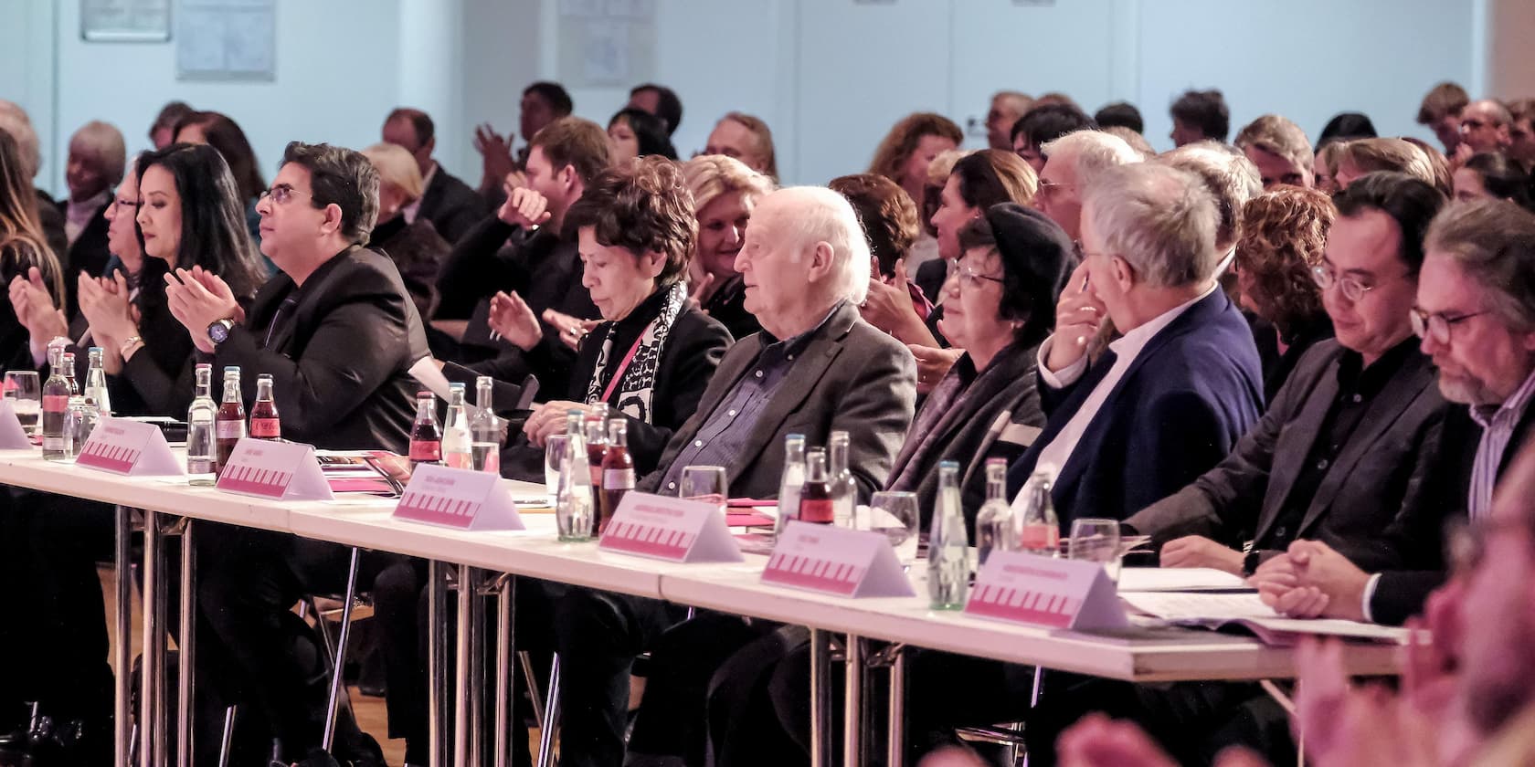 People clapping and sitting at an event in a conference room.