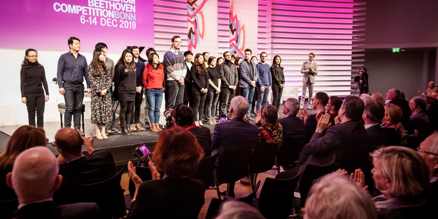 Participants of the Beethoven Competition Bonn 2019 stand on stage while the audience applauds.