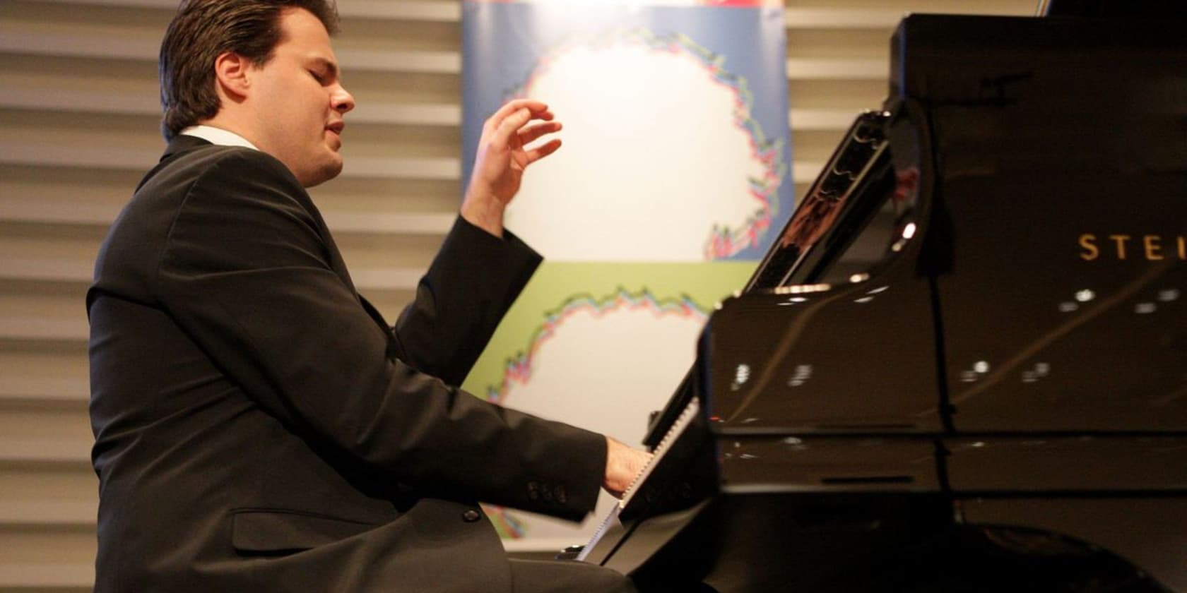 A man in a suit passionately playing the piano on a stage.