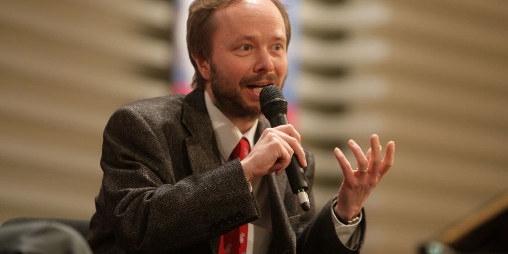 Man in a suit speaking into a microphone at a conference or event.