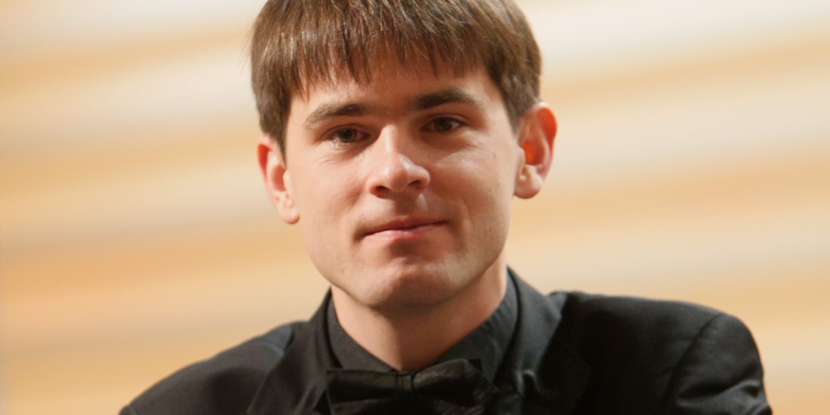 Portrait of a man with short brown hair and a black suit, looking forward.