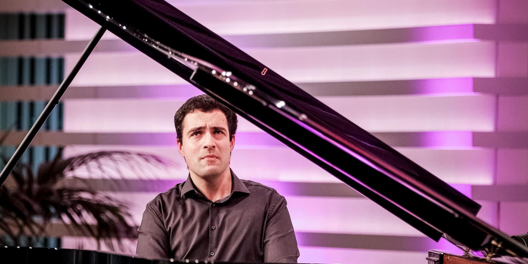 A man playing the piano on a stage with a purple and white illuminated background.