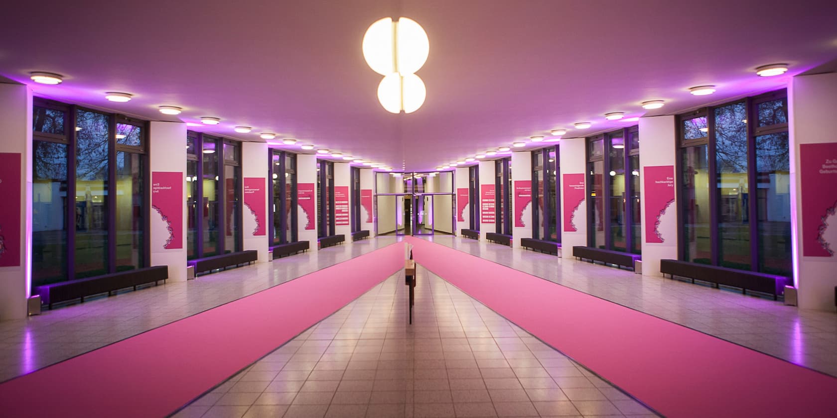 Long, narrow corridor with glass windows and pink lighting.