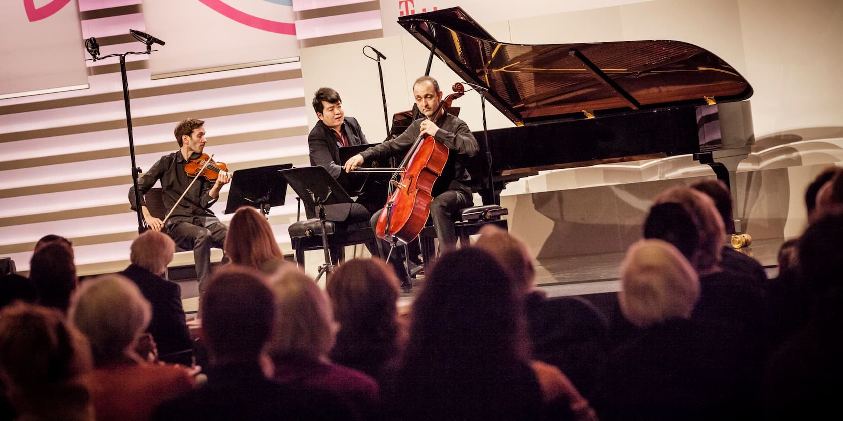 Trio of musicians with a violinist, cellist, and pianist performing in front of an audience.