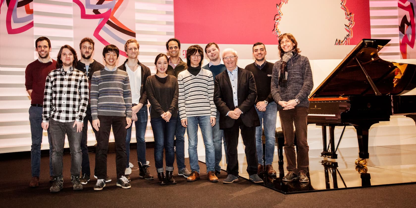 Group of people standing and smiling in front of a grand piano in a modern room.