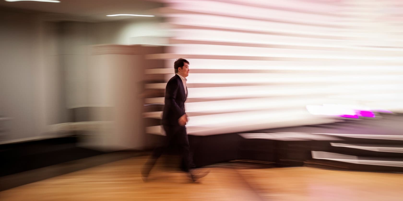 Man in a suit walking quickly along a curved, white-lit wall.