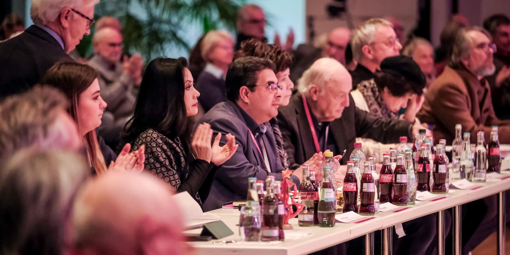 Menschen sitzen an Tischen und applaudieren während einer Konferenz.