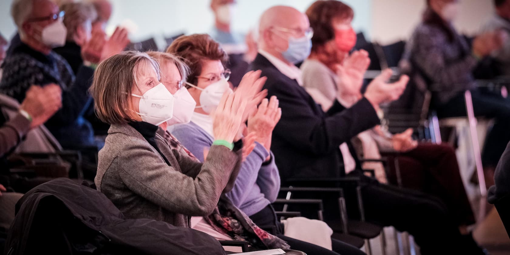 Menschen tragen Gesichtsmasken und applaudieren während einer Veranstaltung.