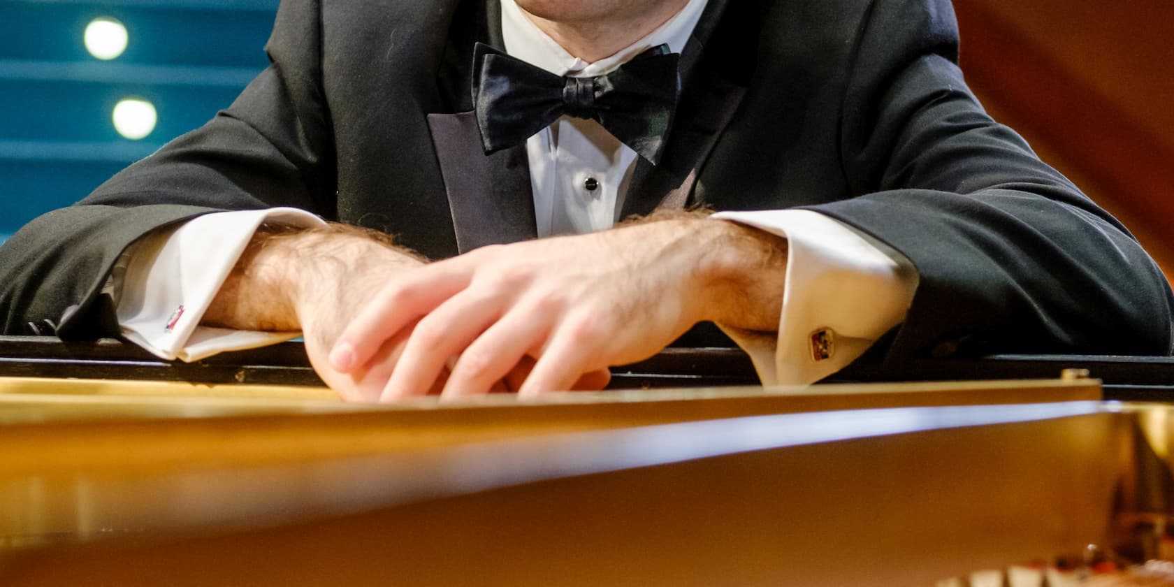 A man in a black tuxedo sits at a piano.