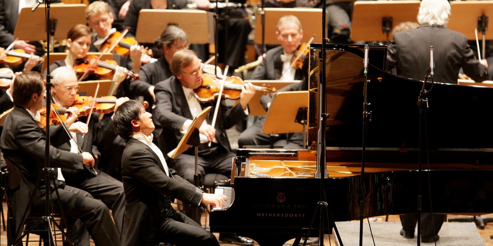 A pianist performs alongside an orchestra with string players at a classical concert.