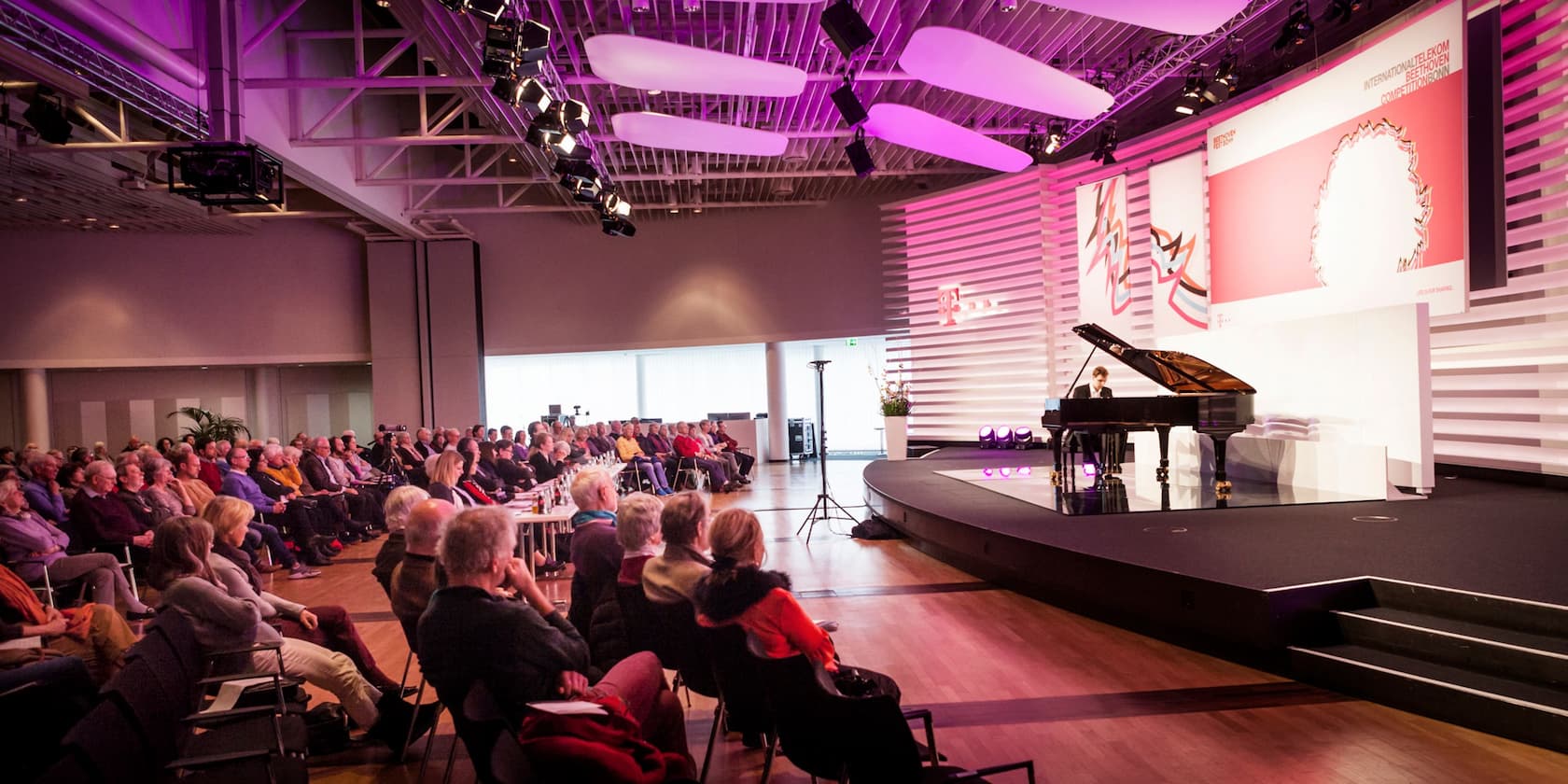 Ein Pianist spielt bei einer Veranstaltung für ein sitzendes Publikum.