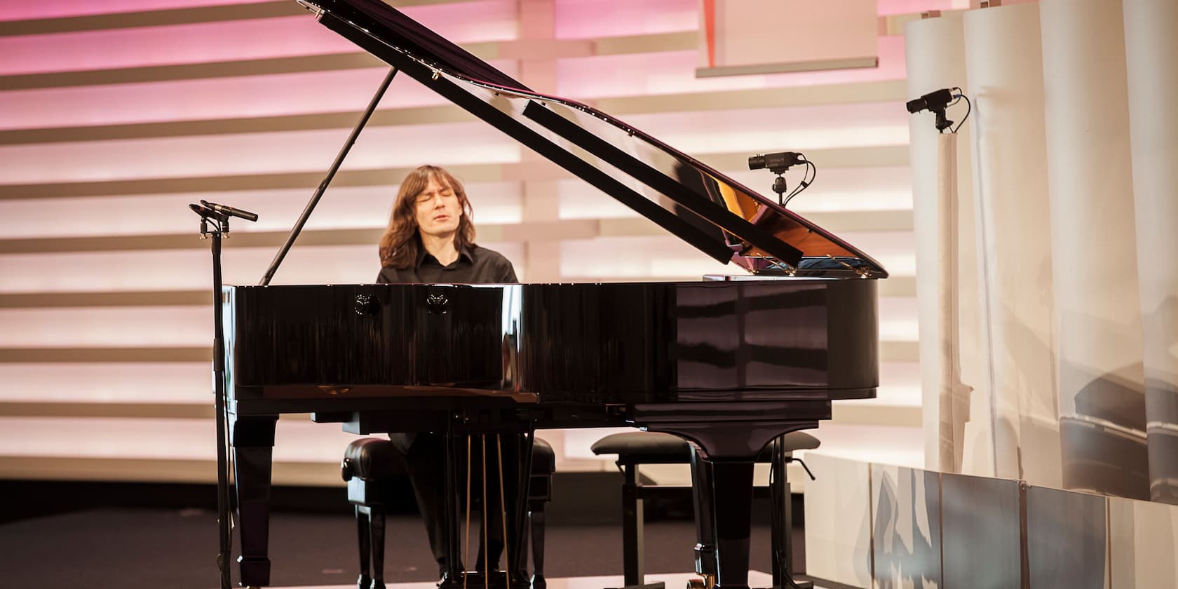 A musician plays a large black grand piano on a stage.