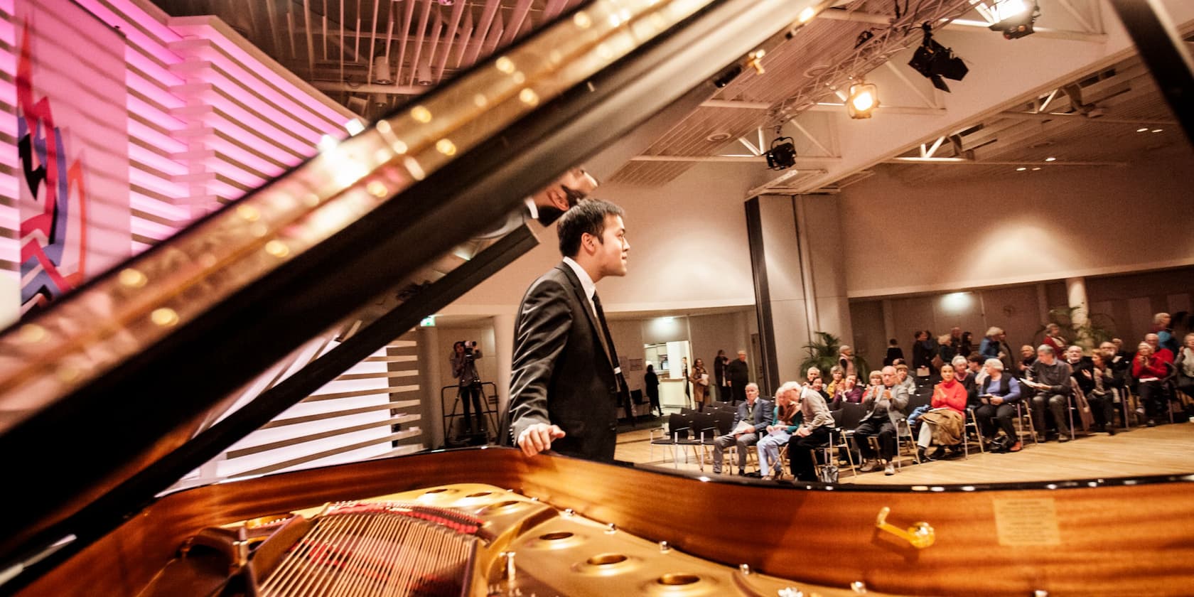 A pianist bows to the audience in a concert hall, with a grand piano in the foreground.