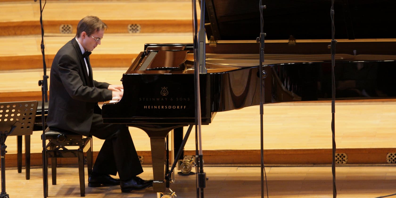 A pianist in a black suit plays the piano on a stage.