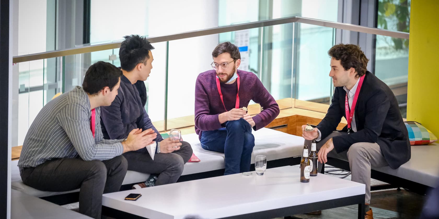 Four men are talking in a lounge area with drinks.