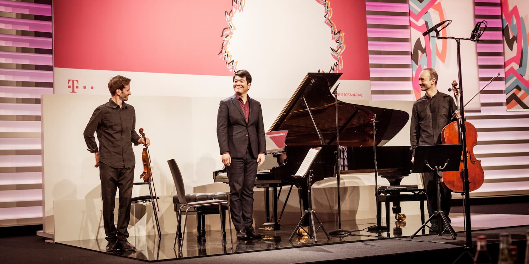 Three musicians on stage with a piano, a violin, and a cello during a performance