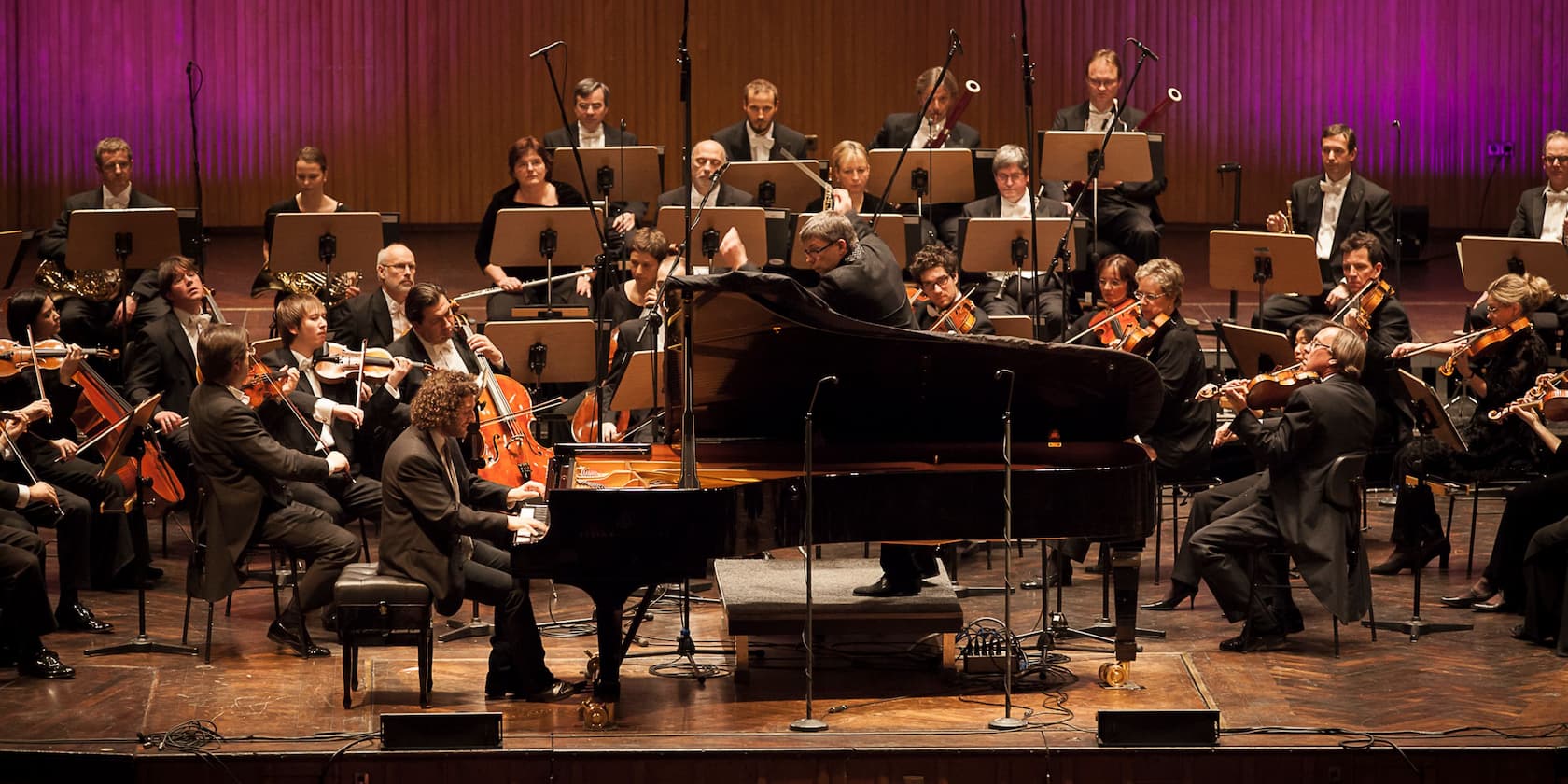 An orchestra is performing on a stage, with a pianist at the piano in the foreground.