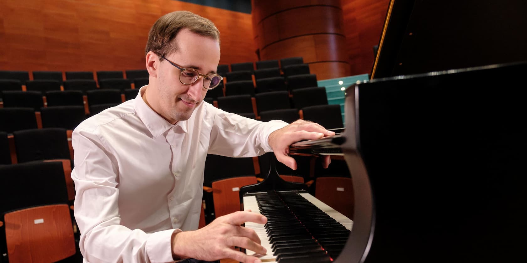 Ein Mann spielt Klavier auf einer Bühne in einem leeren Auditorium.