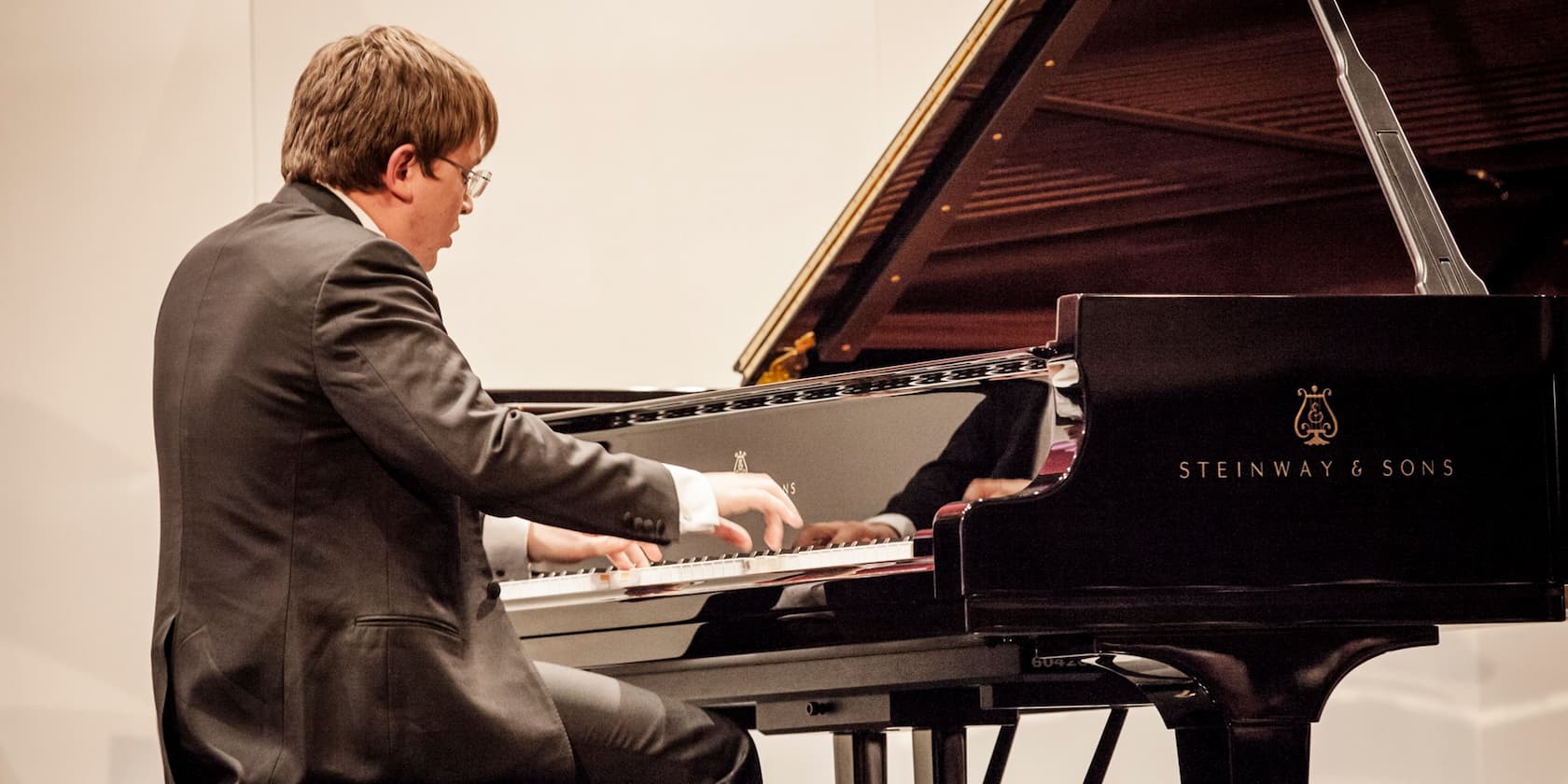 A man in a suit is playing a black Steinway & Sons grand piano.