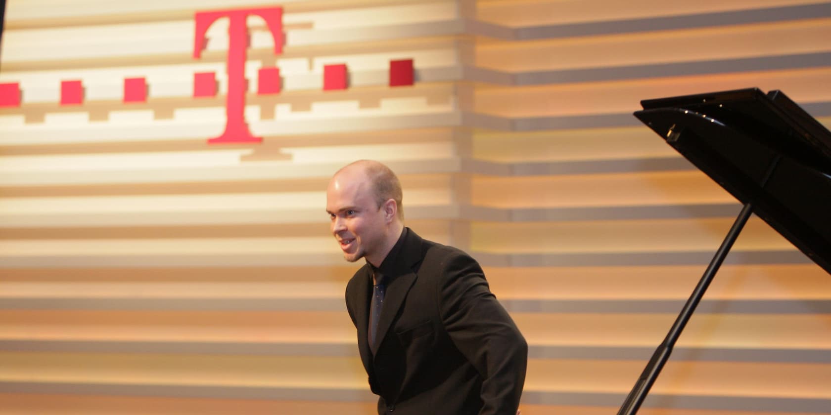 Man in a black suit in front of a background with the Telekom logo and a piano