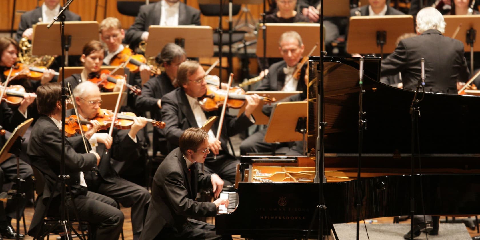 Ein Orchester spielt während eines Konzerts. Ein Pianist sitzt am Klavier und der Dirigent steht vor dem Orchester.