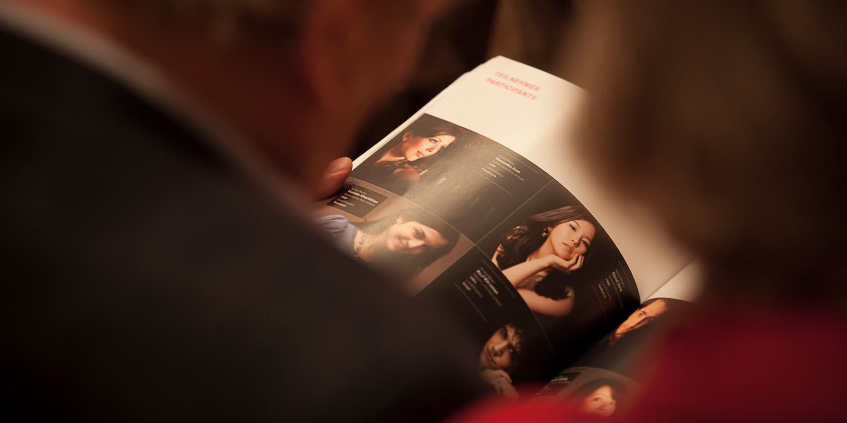 Two people looking at a magazine featuring profile pictures and descriptions of participants.