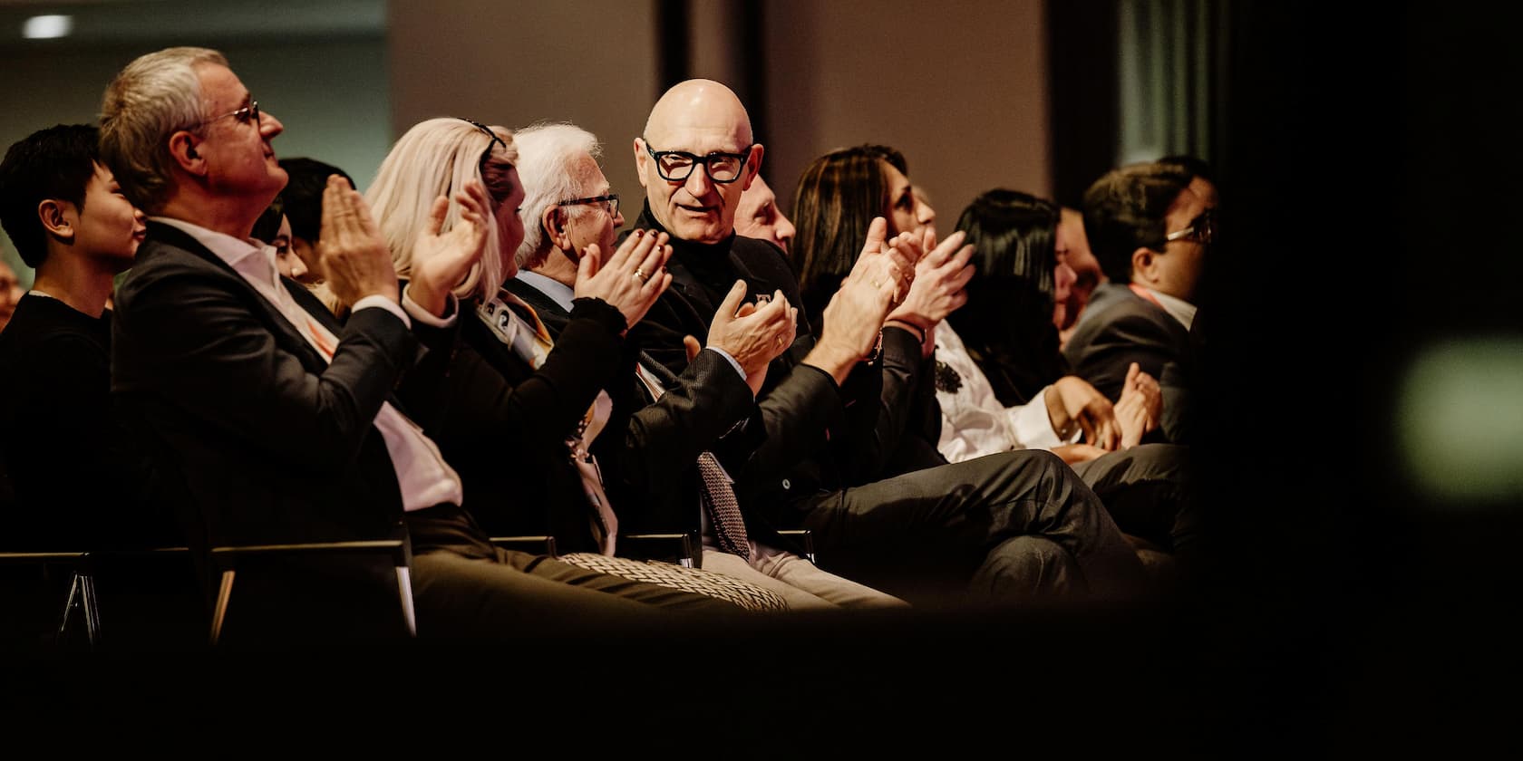 People in formal attire clapping during an event.