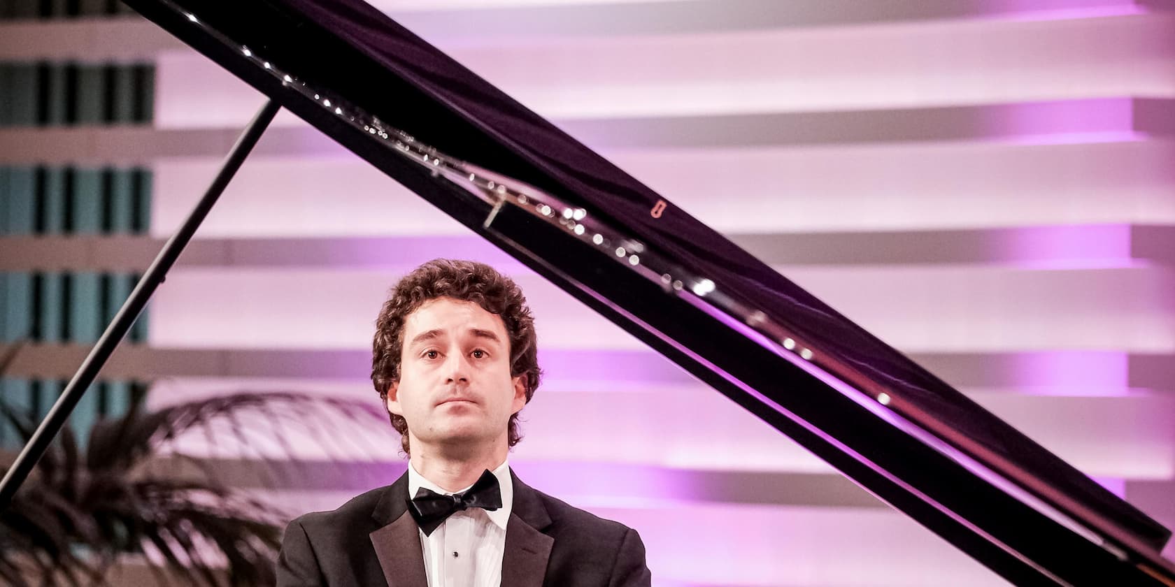 Man in a suit playing piano on a stage with purple backlighting.