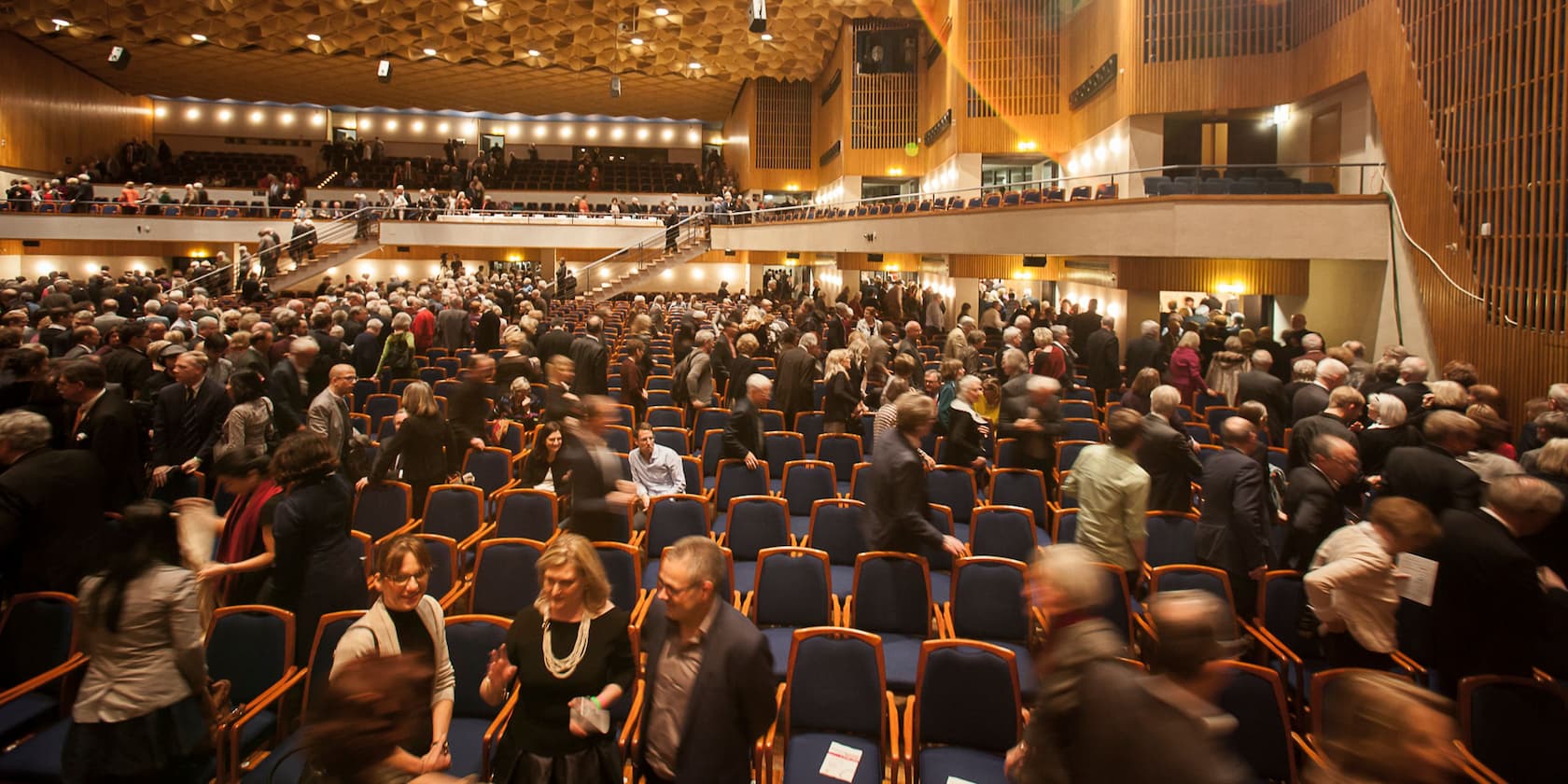 People gathering in a large hall with tiered seating, seemingly before or after an event.