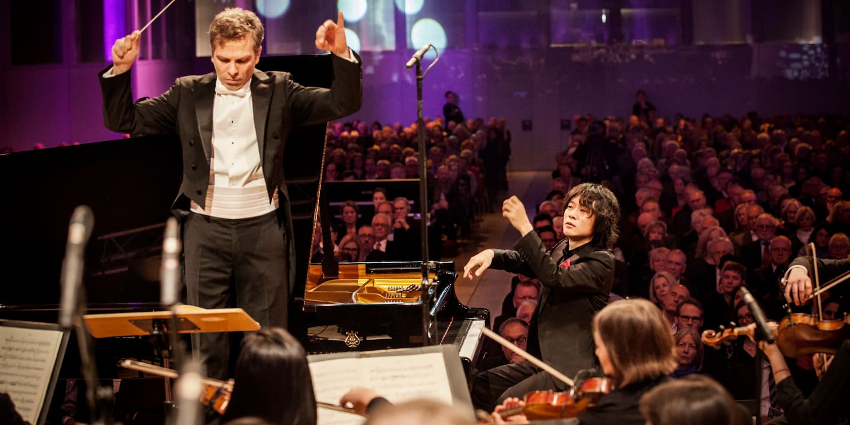 Conductor and pianist performing with an orchestra in front of an audience.