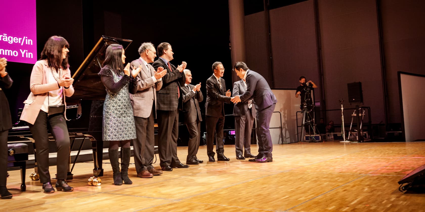 A group of people standing on a stage, applauding a man who is receiving an award.