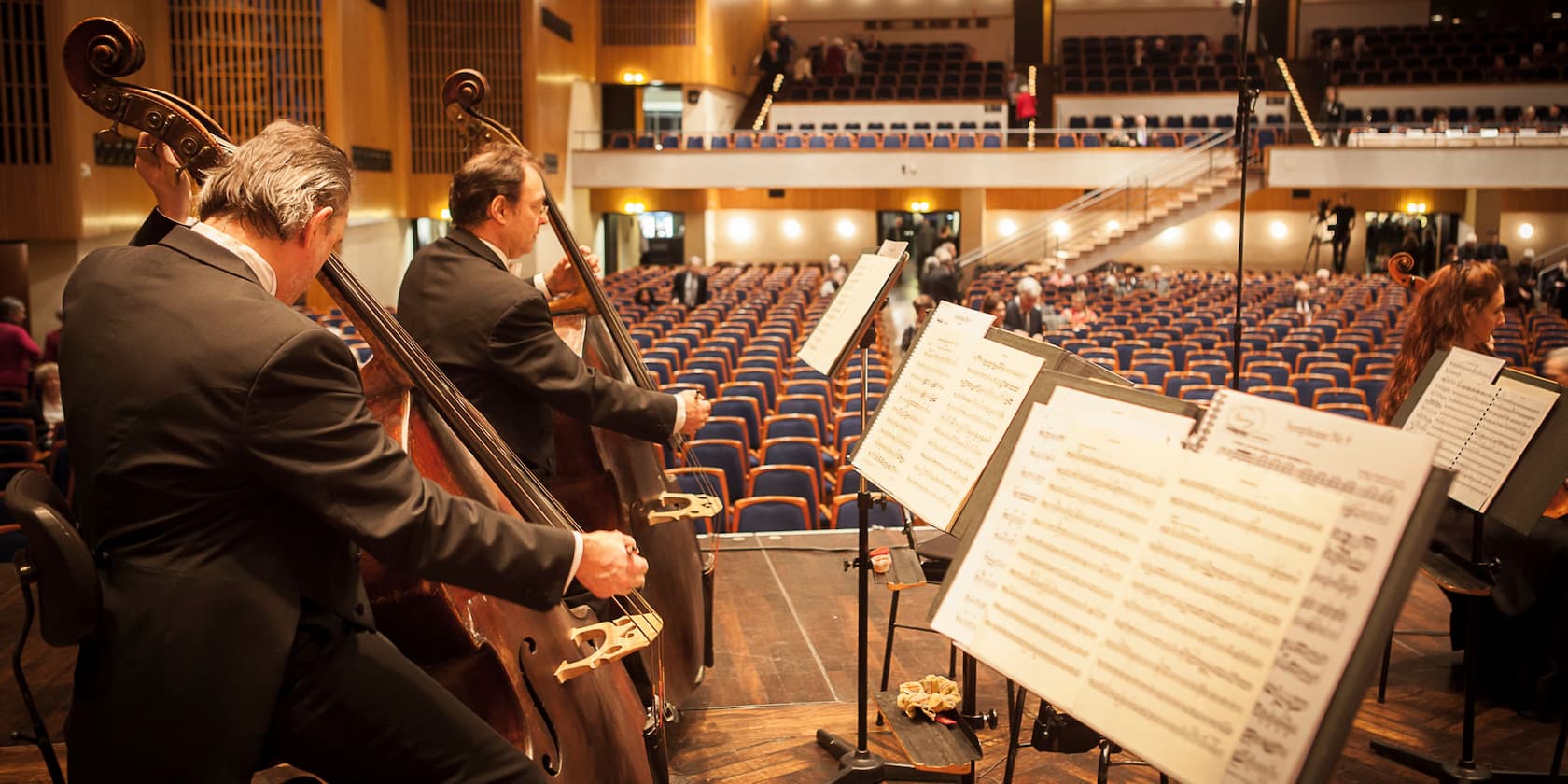 Musicians tuning their instruments on stage in an empty concert hall.