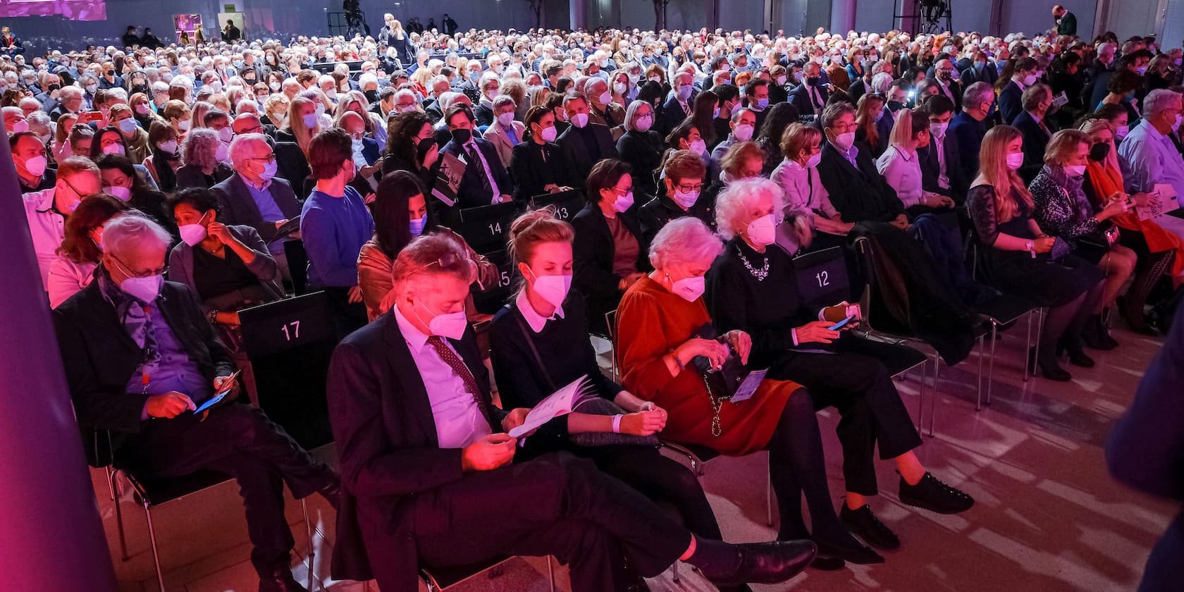 A large crowd of people seated at an event, many wearing face masks.