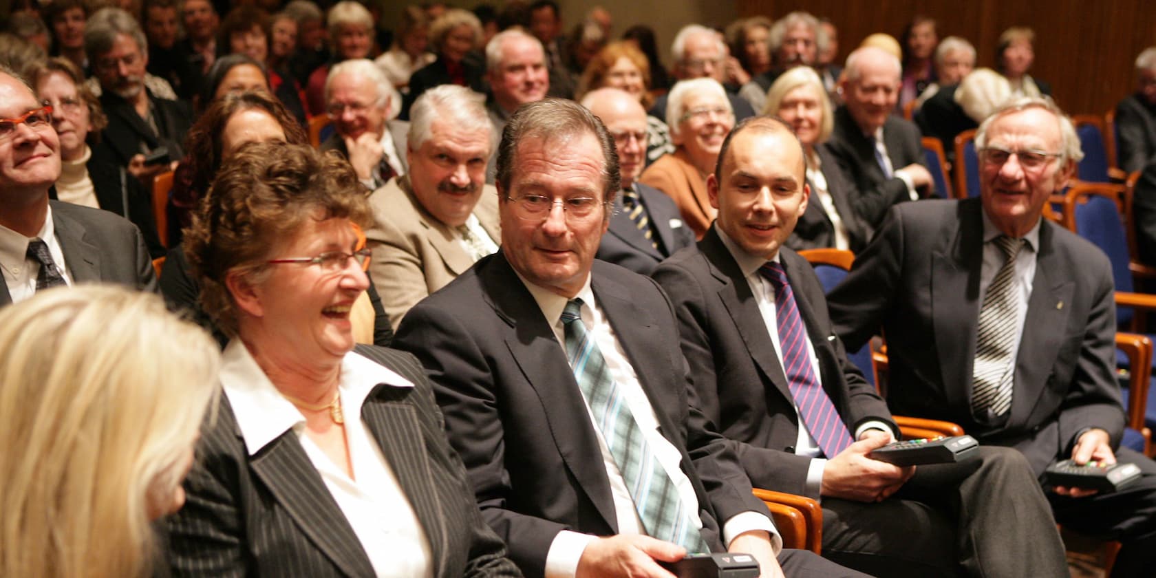 A group of people in formal attire sitting next to each other and smiling at an event.