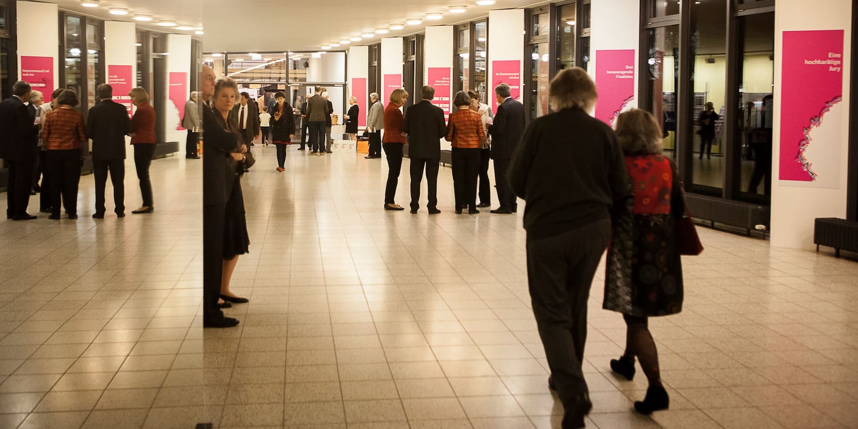 People standing in an exhibition hall with pink posters on the walls.