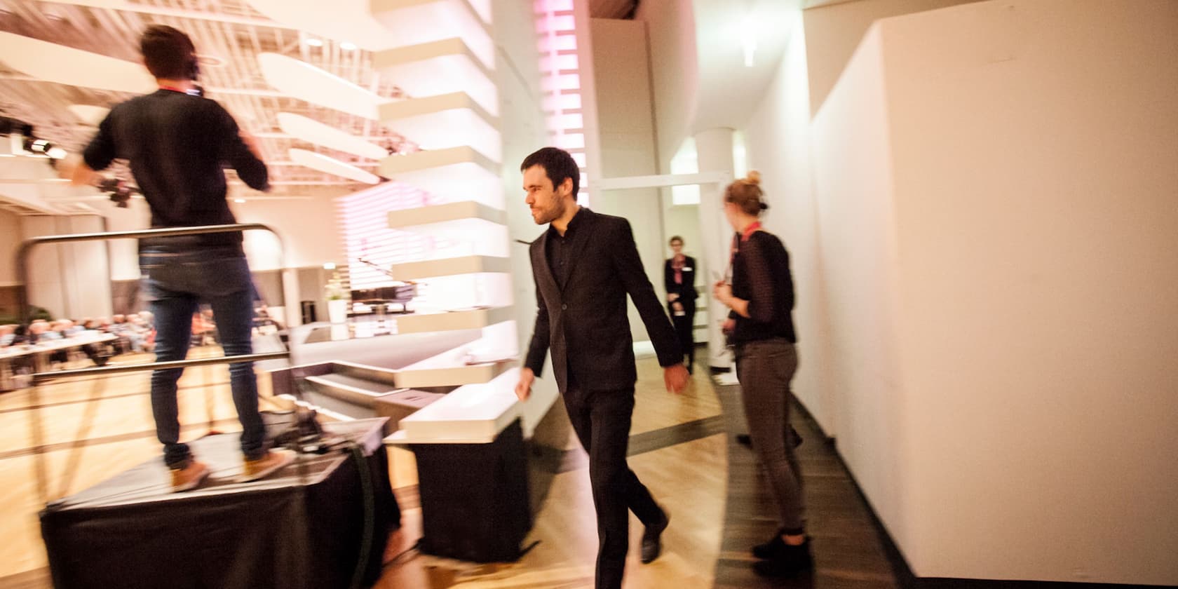 Man in a black suit walking through a modern event space.