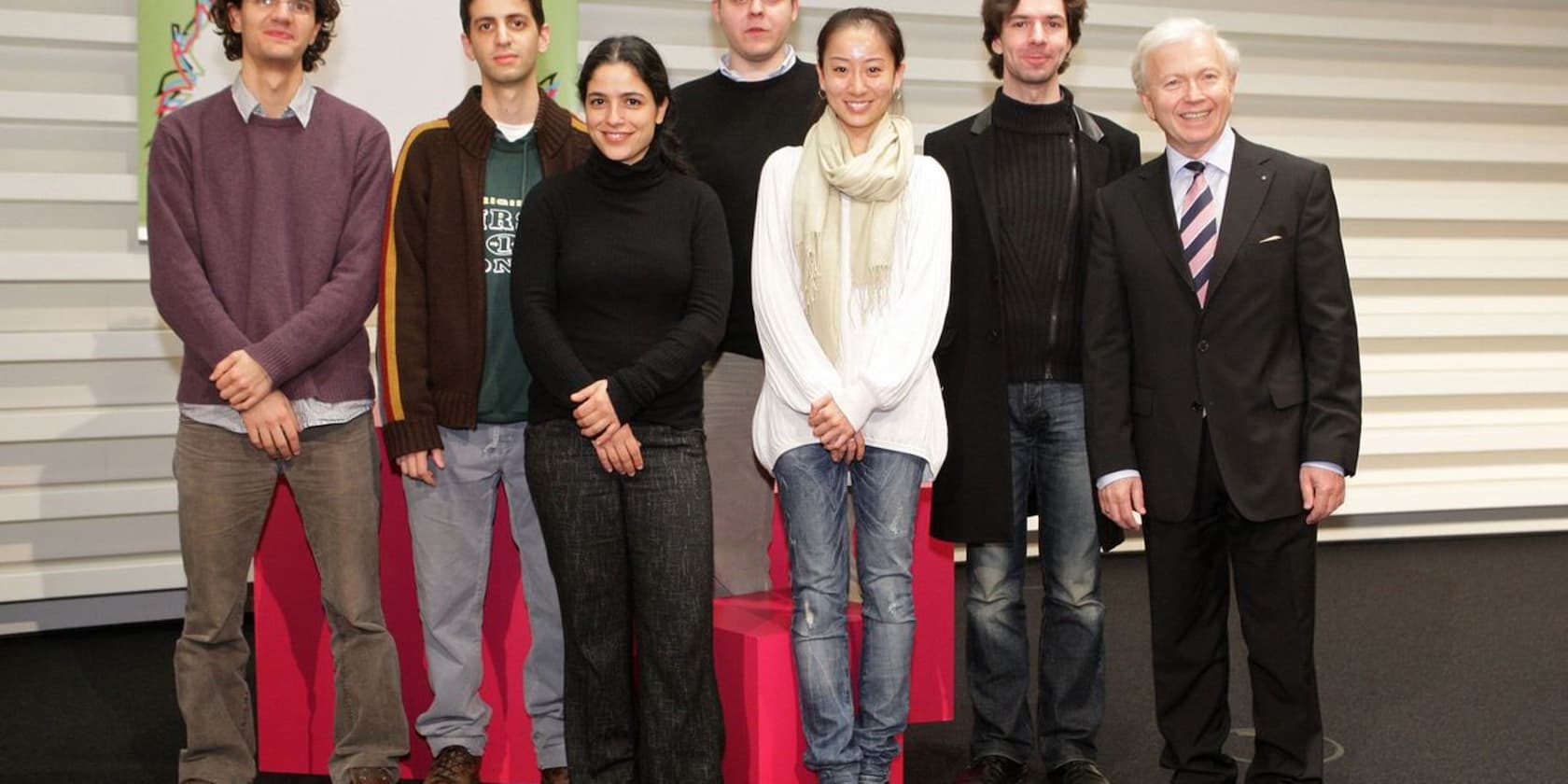 Seven people stand together for a group photo, including a man in a suit.