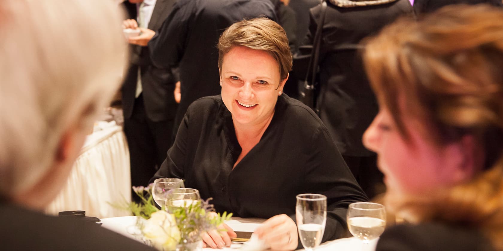 Woman in black clothing smiling at a social event.