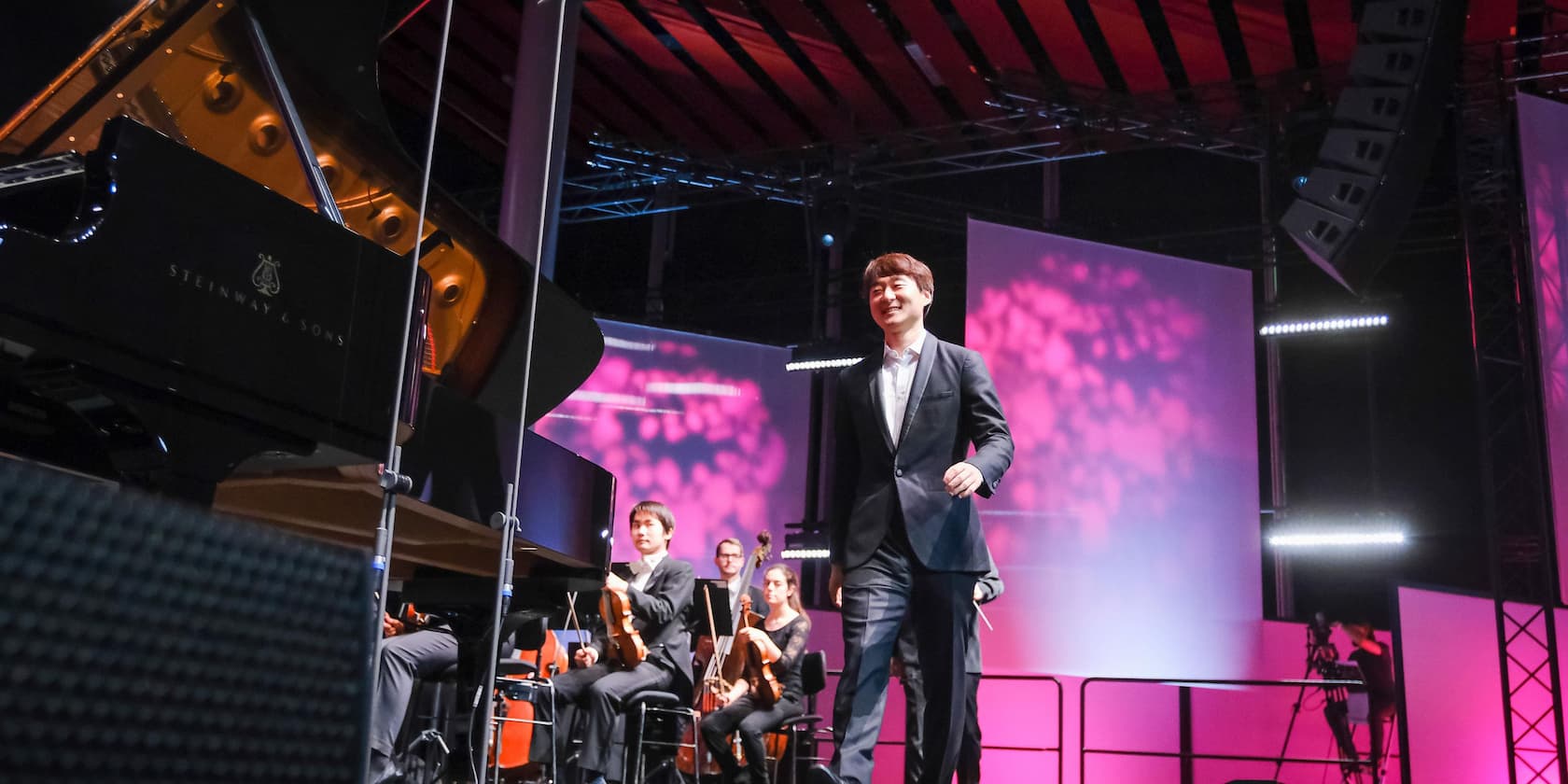 A pianist walks onto the stage while the orchestra sits ready to play. A large Steinway & Sons grand piano is in the foreground.