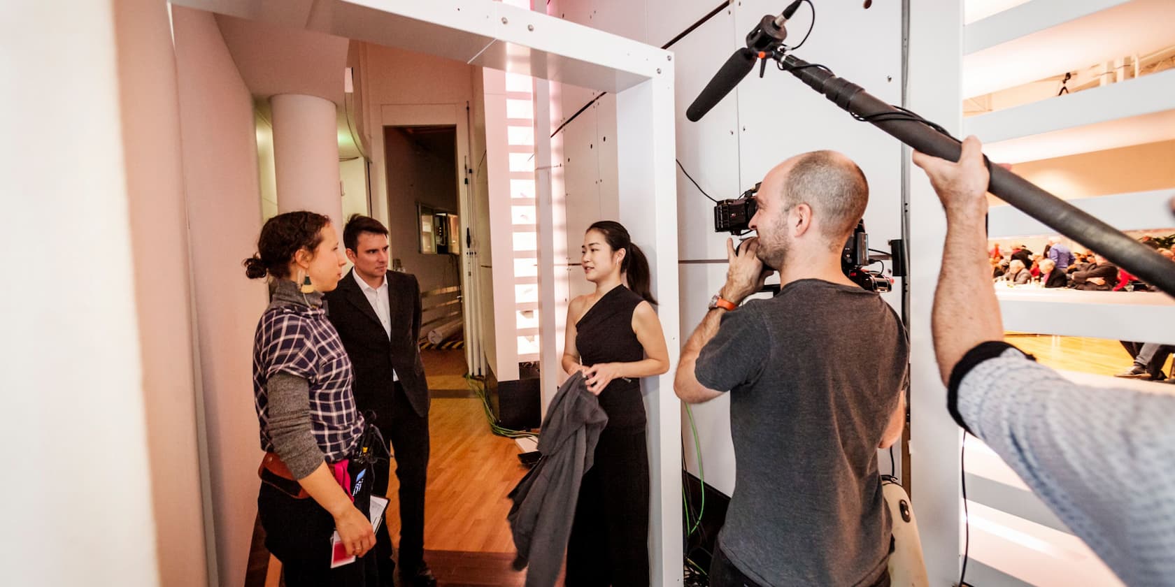 A woman in a black dress takes part in a backstage interview with a cameraman and a boom operator working.