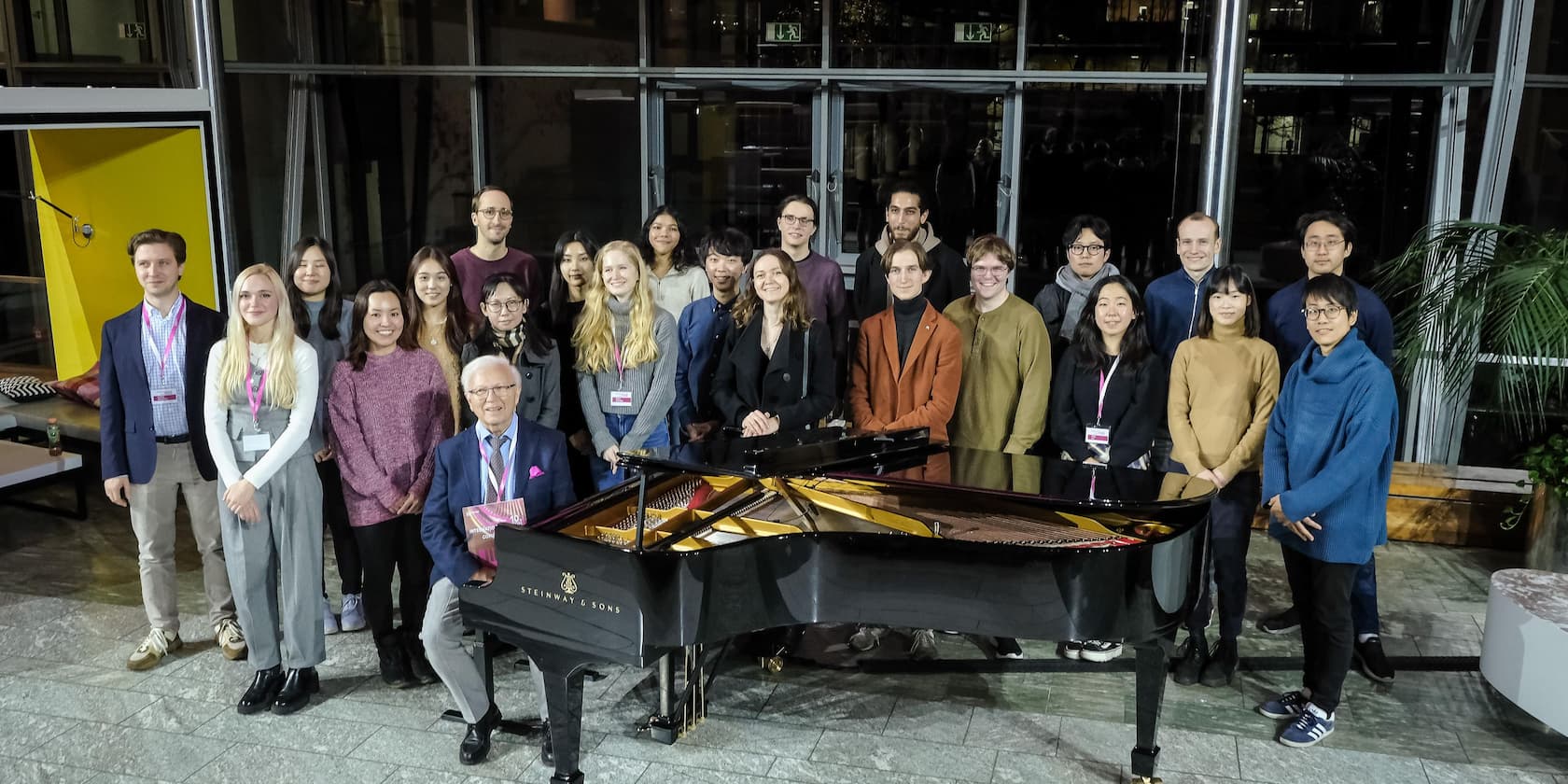 Group of people posing behind a black grand piano.