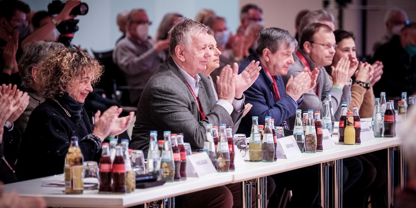 Several people sitting at a table clapping, with various drinks in front of them.