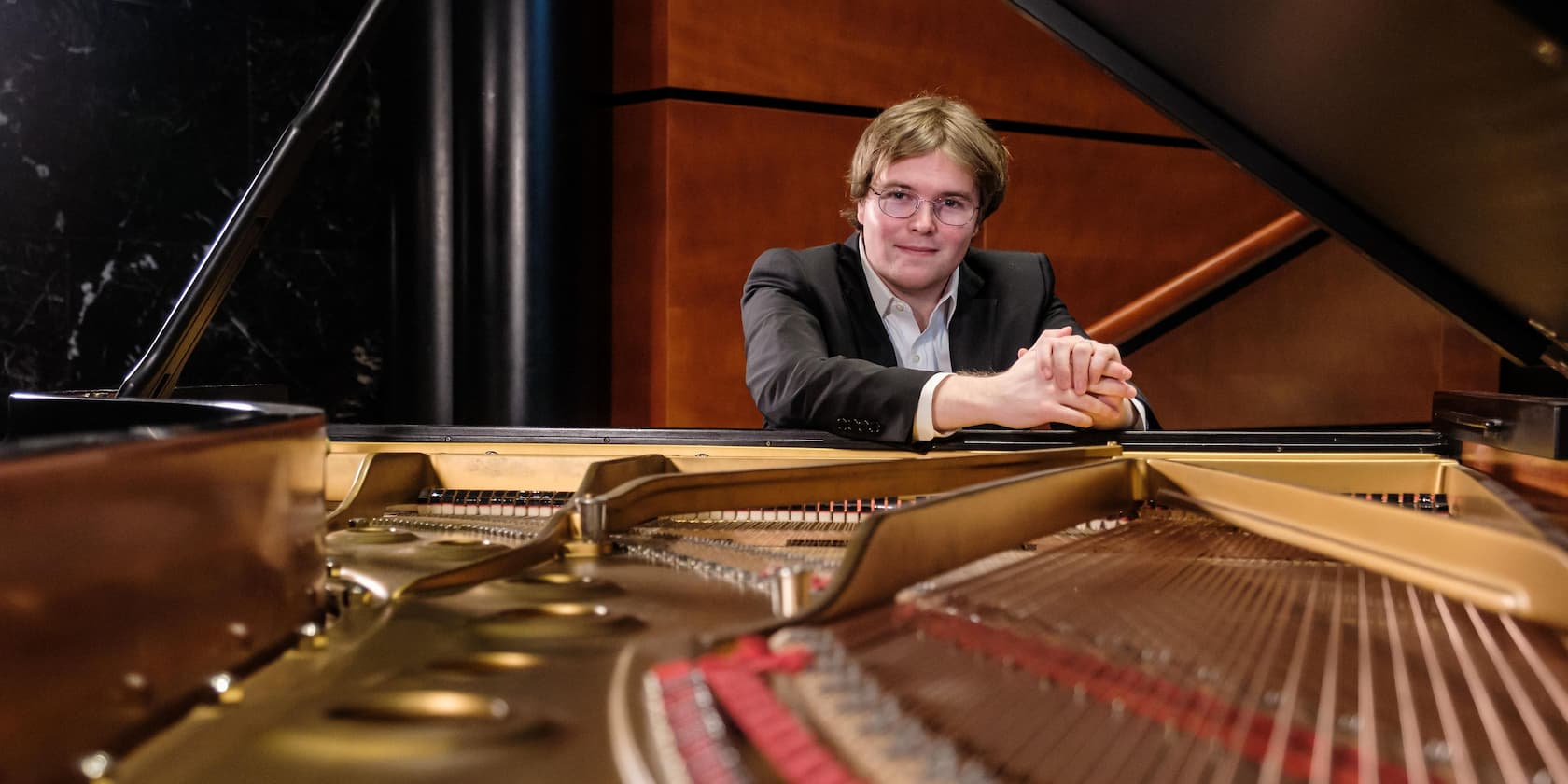 A man leaning on a grand piano with the lid open.