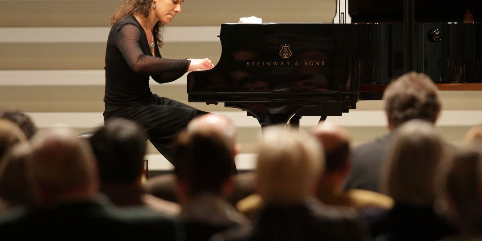 A woman playing piano on a stage before an audience.