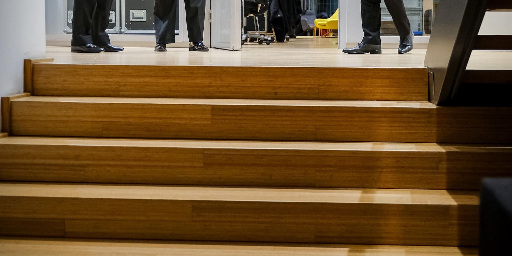 Wooden staircase in an office building, with only the legs of three people in suits visible